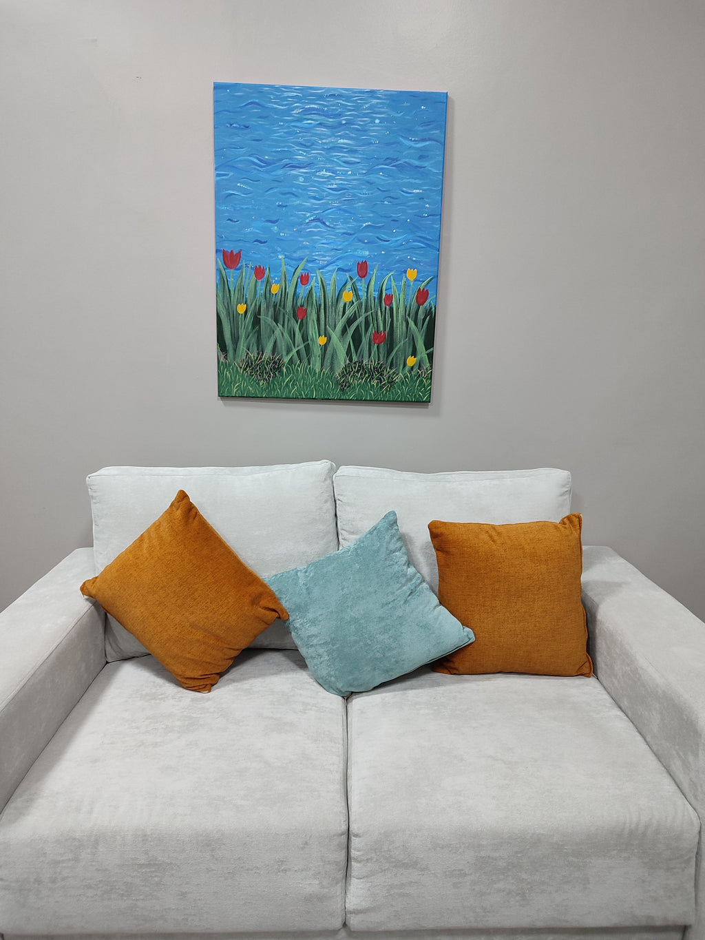 Gray sofa with orange and blue pillows, featuring a colorful painting of flowers on a gray wall.