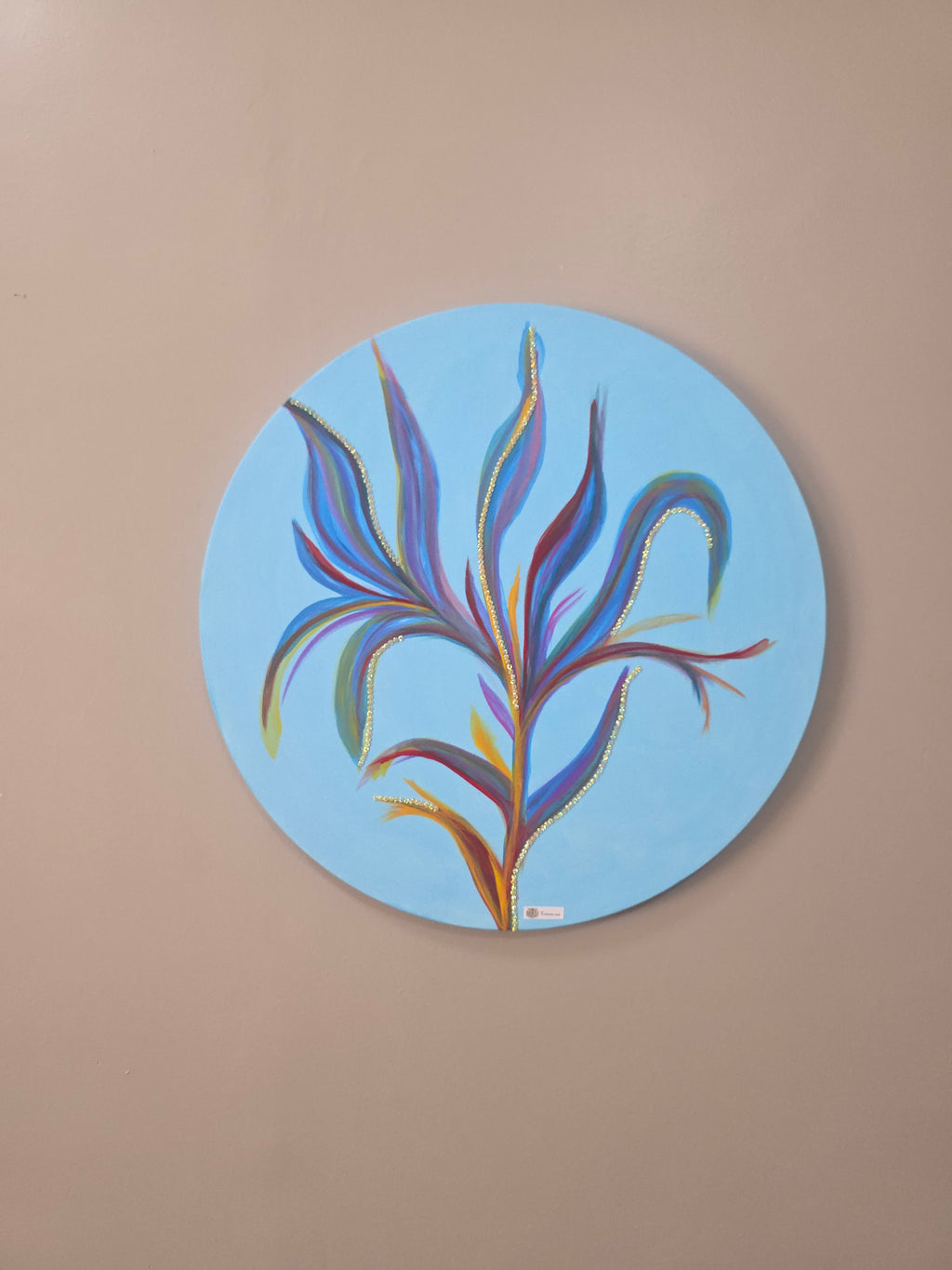 Round abstract painting with colorful leaf-like design on a beige wall