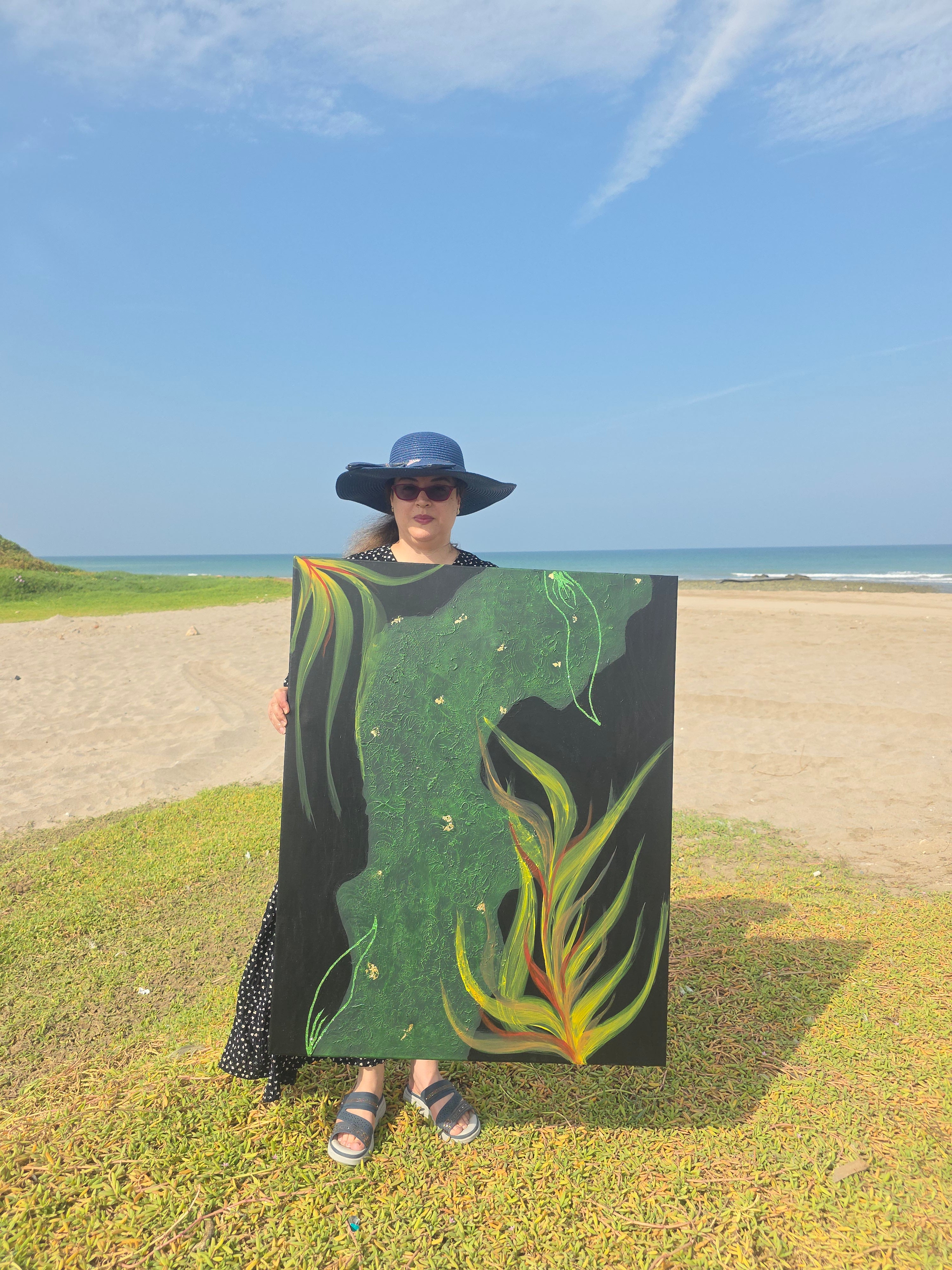 Person holding a large green leaf-shaped object on a grassy field with blue sky.
