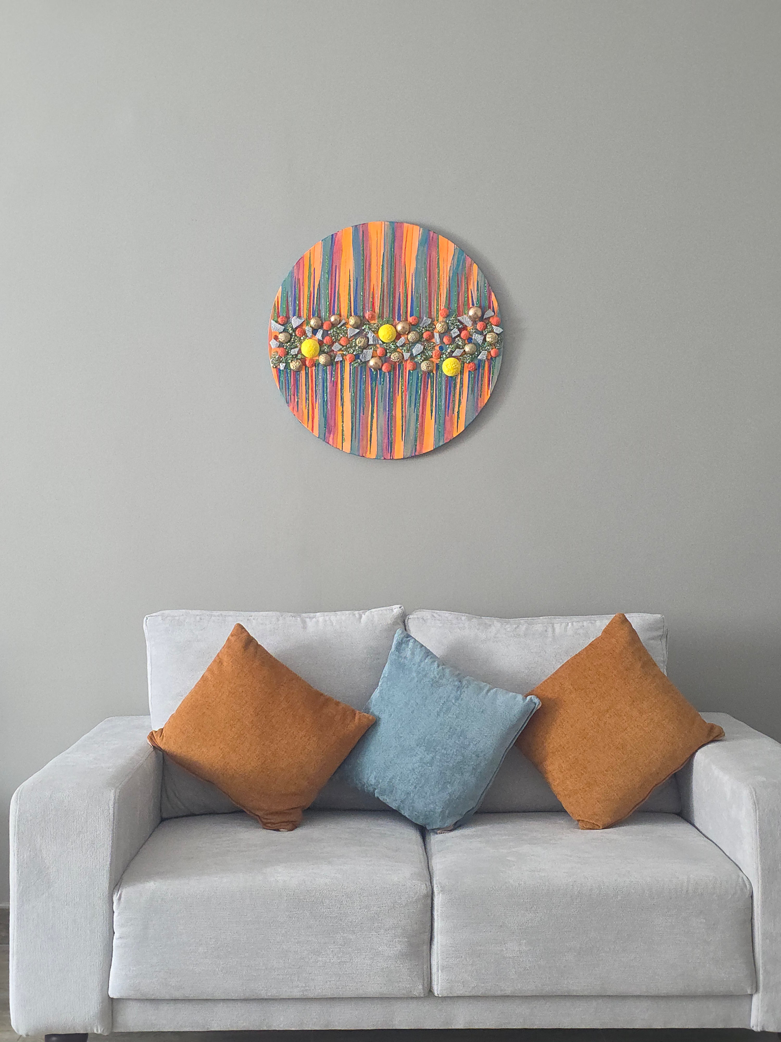 Decorative circular wall piece with colorful abstract design above a gray sofa with patterned cushions.