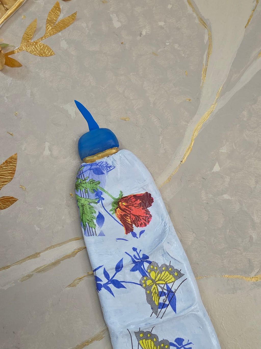 Decorative bottle cover with floral and butterfly design on a marble surface