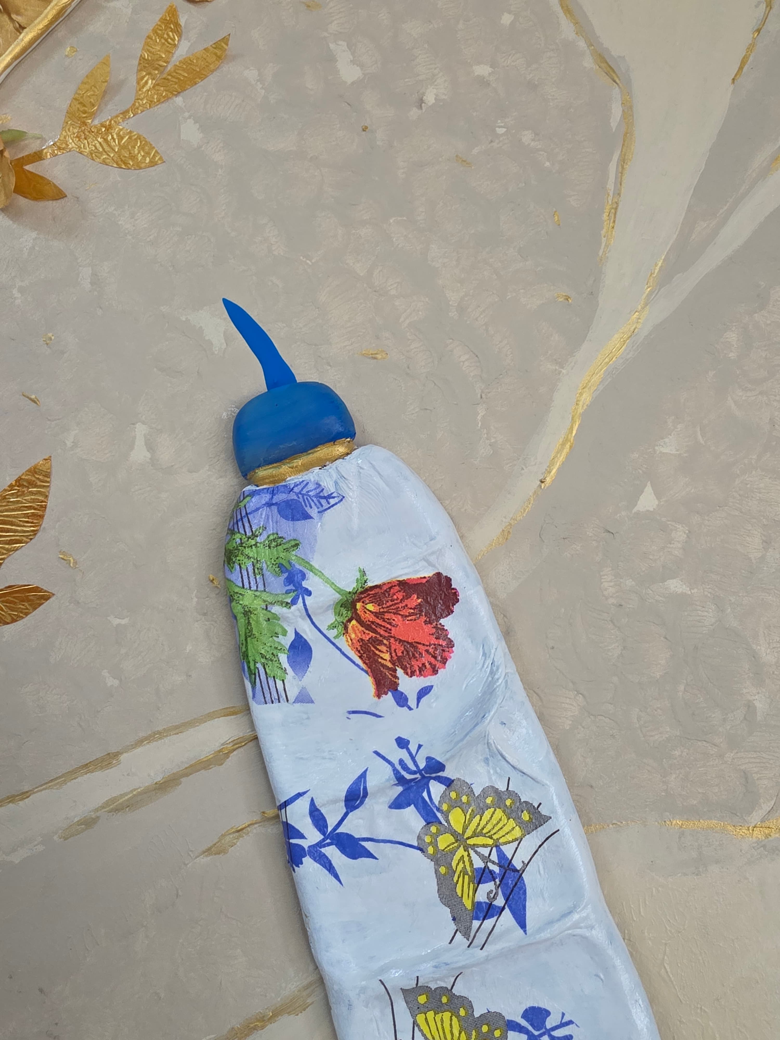 Decorative bottle cover with floral and butterfly design on a marble surface