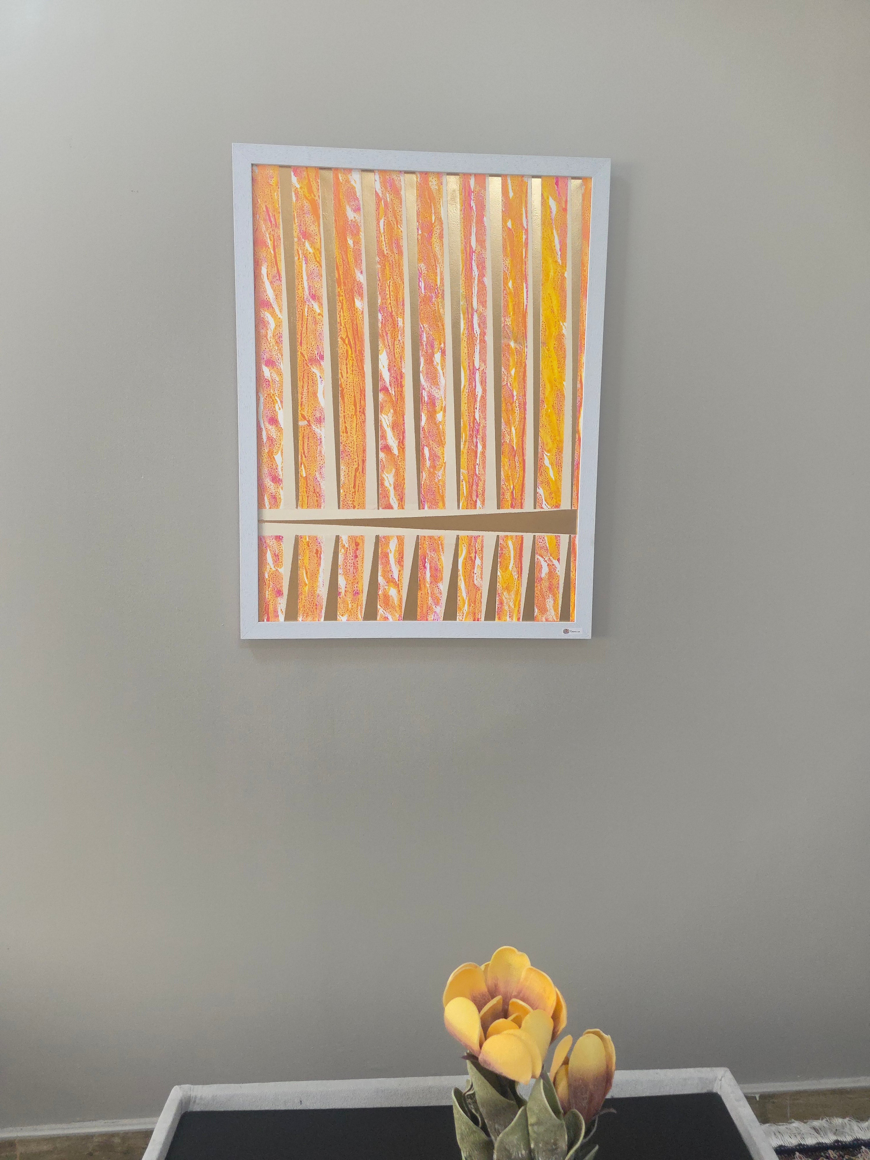 Framed artwork on a gray wall with a vase of yellow flowers to the right.