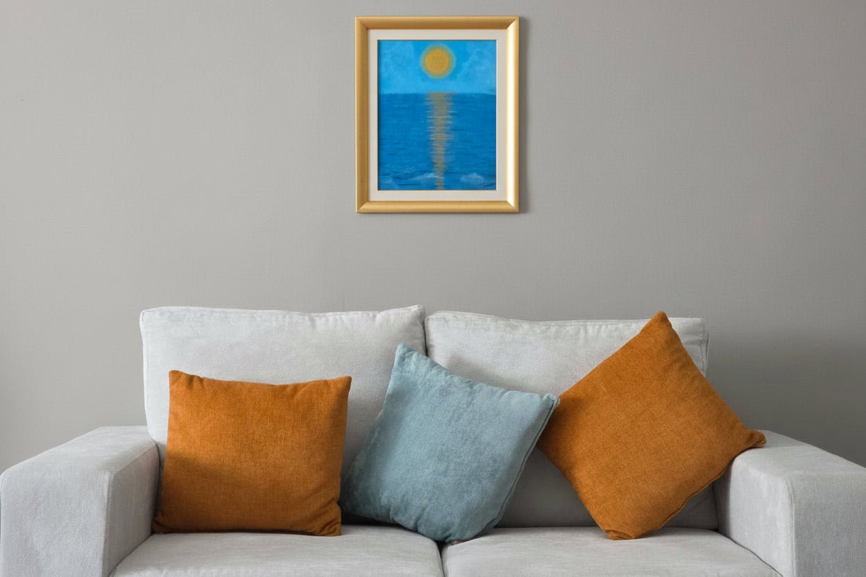 Golden Horizon original sun and sea painting in a gold frame styled above a grey sofa with yellow cushions.