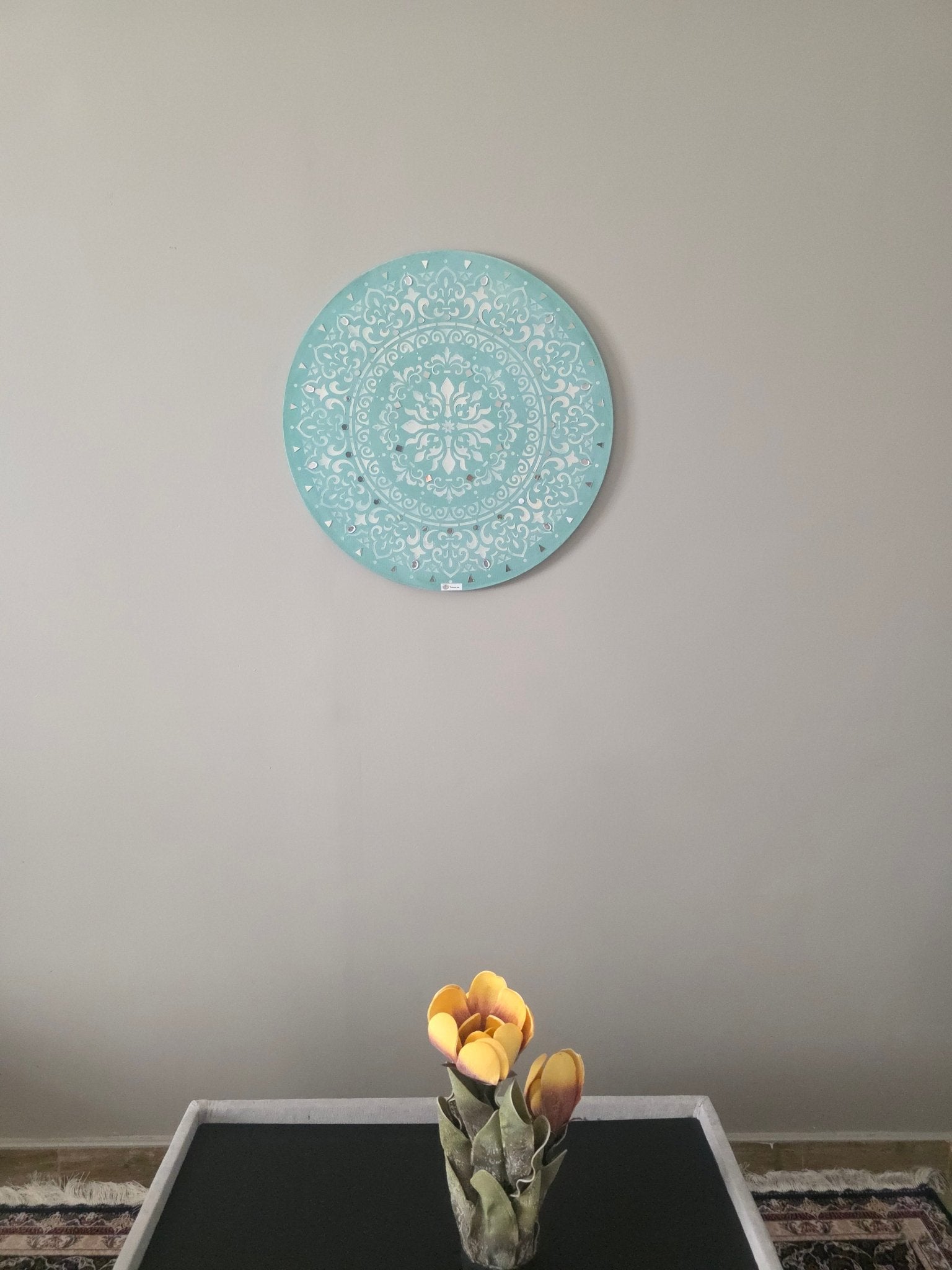 Decorative round turquoise plate on a plain wall with a small plant in the foreground.